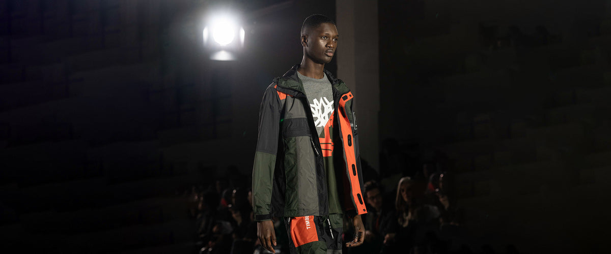 Model on the catwalk in an olive, black and orange Timberland × RÆBURN jacket.