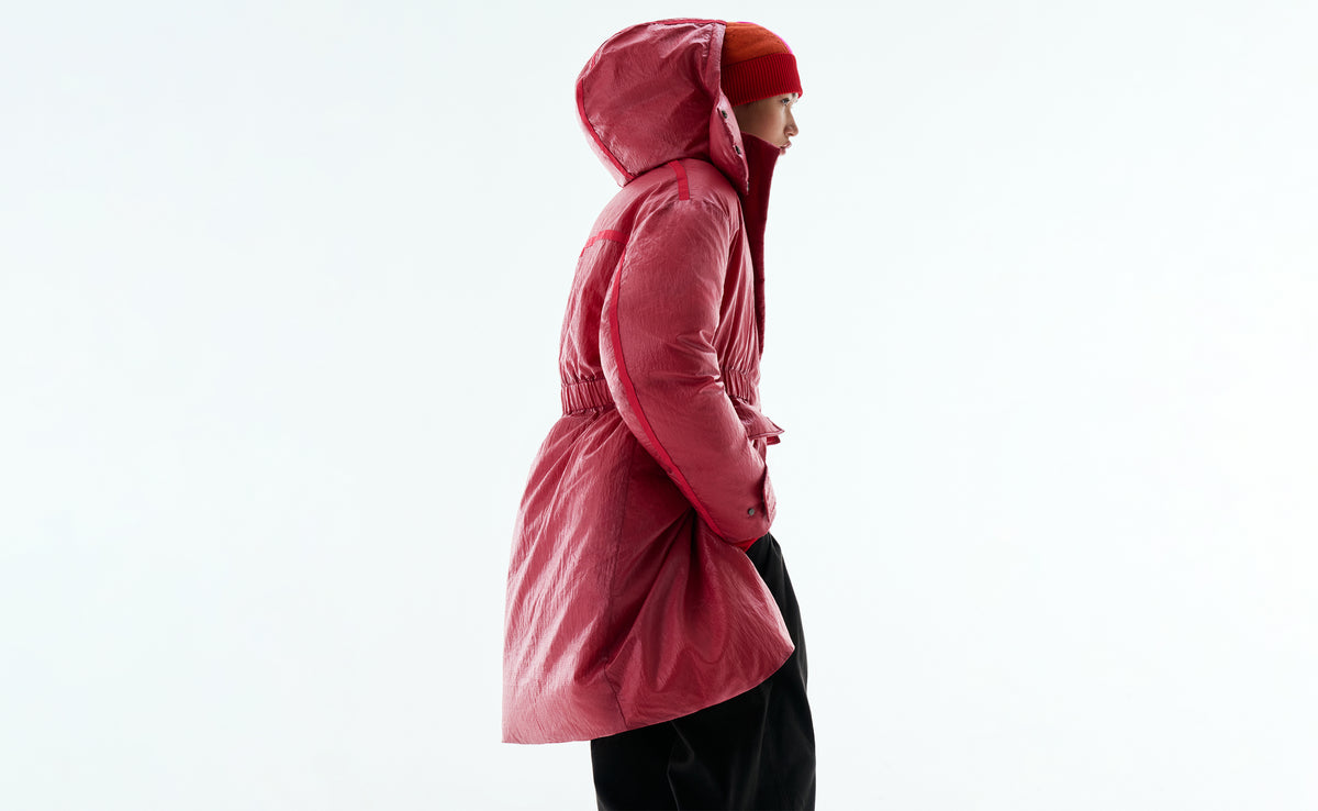 Side view of a model in a hooded cherry-red padded coat and a red beanie.