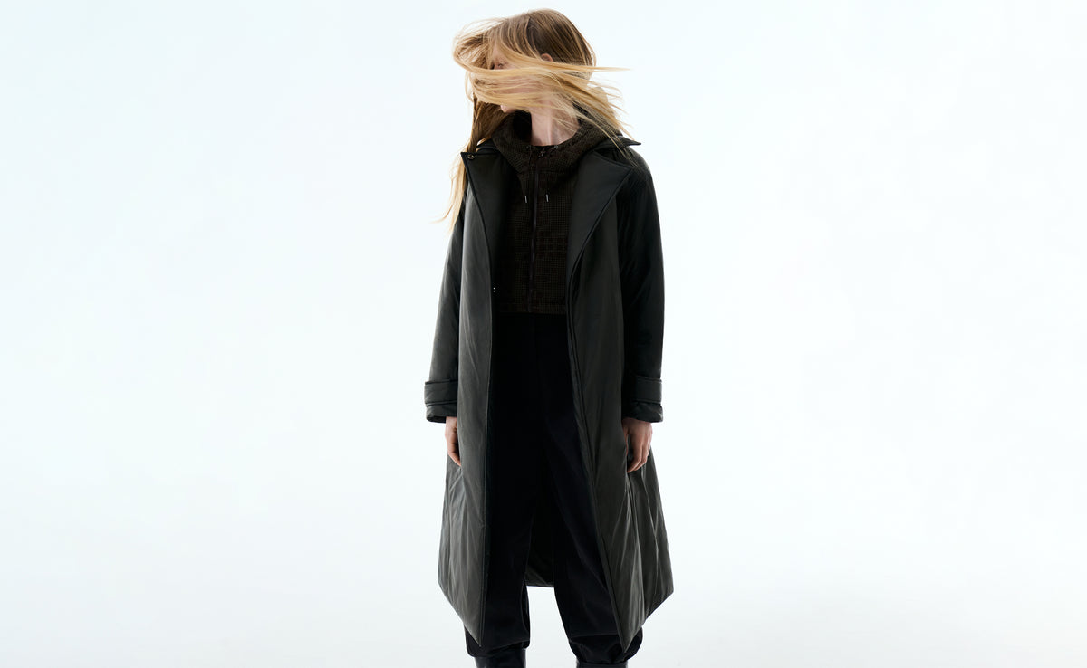 A model with her hair blown across her face in a long black padded coat over a khaki jacquard layer.